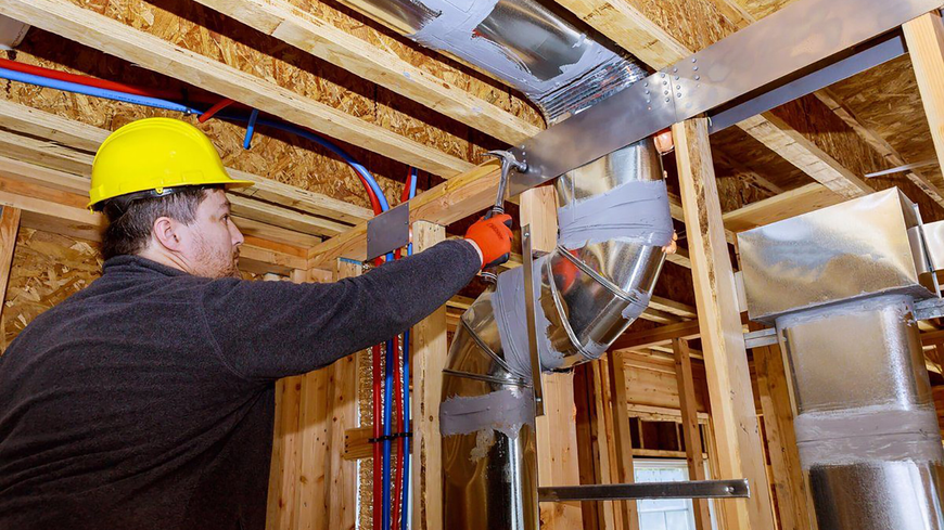 A man wearing a hard hat and gloves is working on the ceiling of a house under construction.