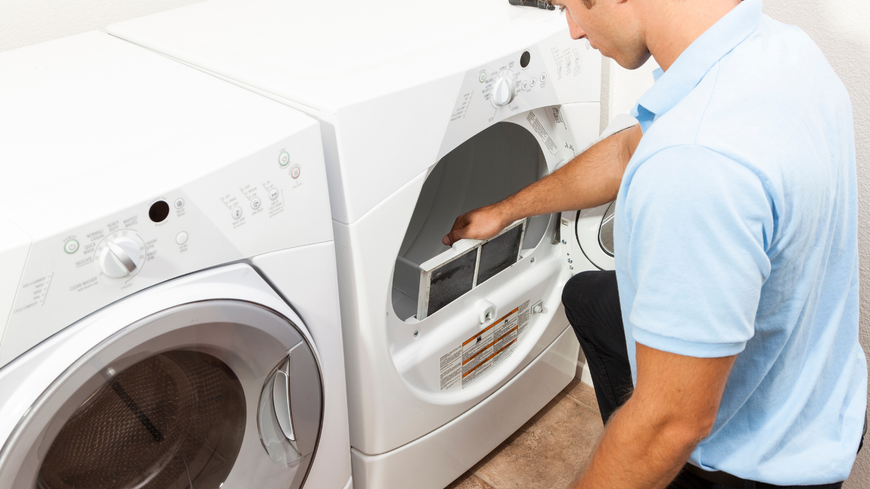 A man is working on a washer and dryer in a laundry room.
