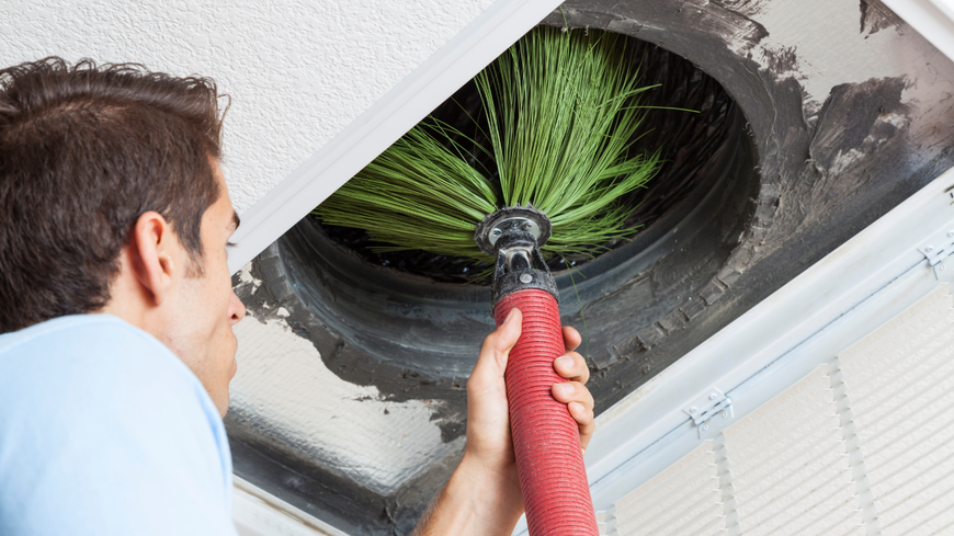 A man is cleaning an air vent with a brush.