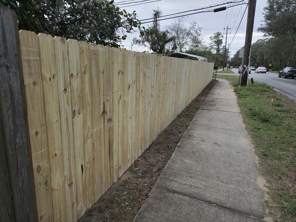 Wooden fence alongside a sidewalk and road; overcast sky.