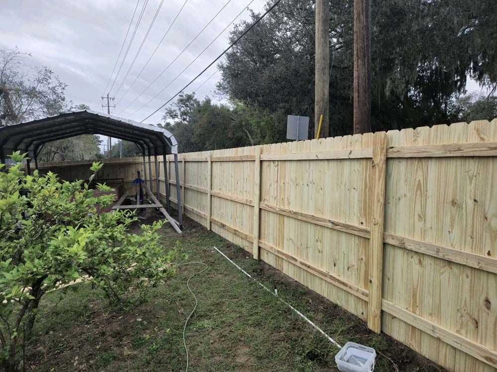 A newly built wooden fence in a backyard, beside a covered car port.