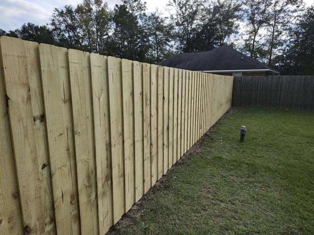 Wooden privacy fence in a backyard, with grass and trees in the background.