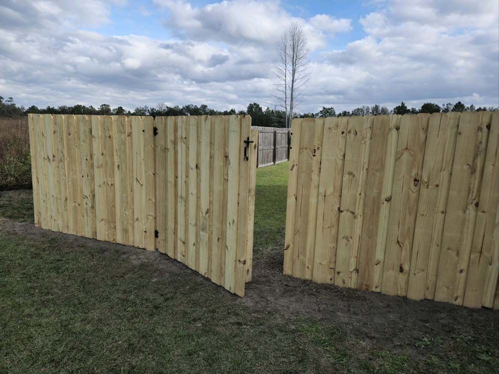 Wooden fence with an opening on a grassy field under a cloudy sky.