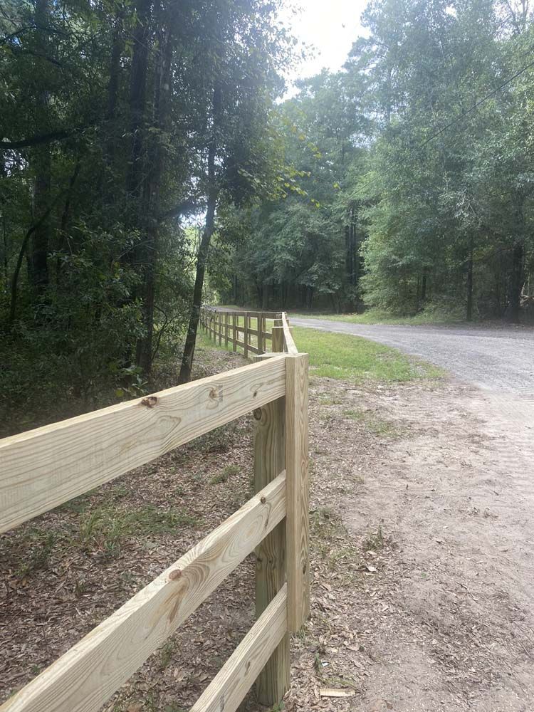 Wooden fence alongside a dirt road in a wooded area.