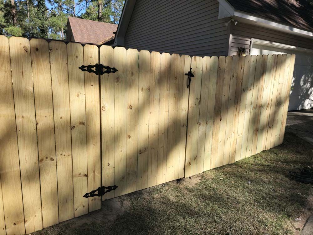 Wooden fence with gate, featuring black hinges and latch, in front of a house.