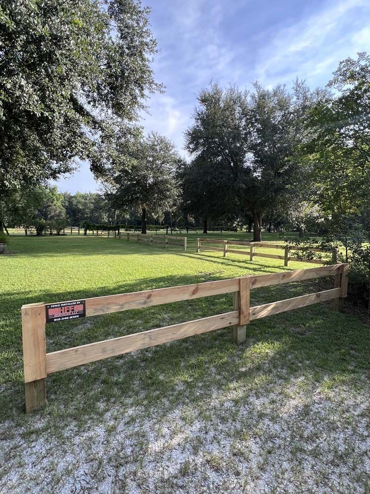 A wooden fence encloses a grassy area with trees and a cloudy sky. A 