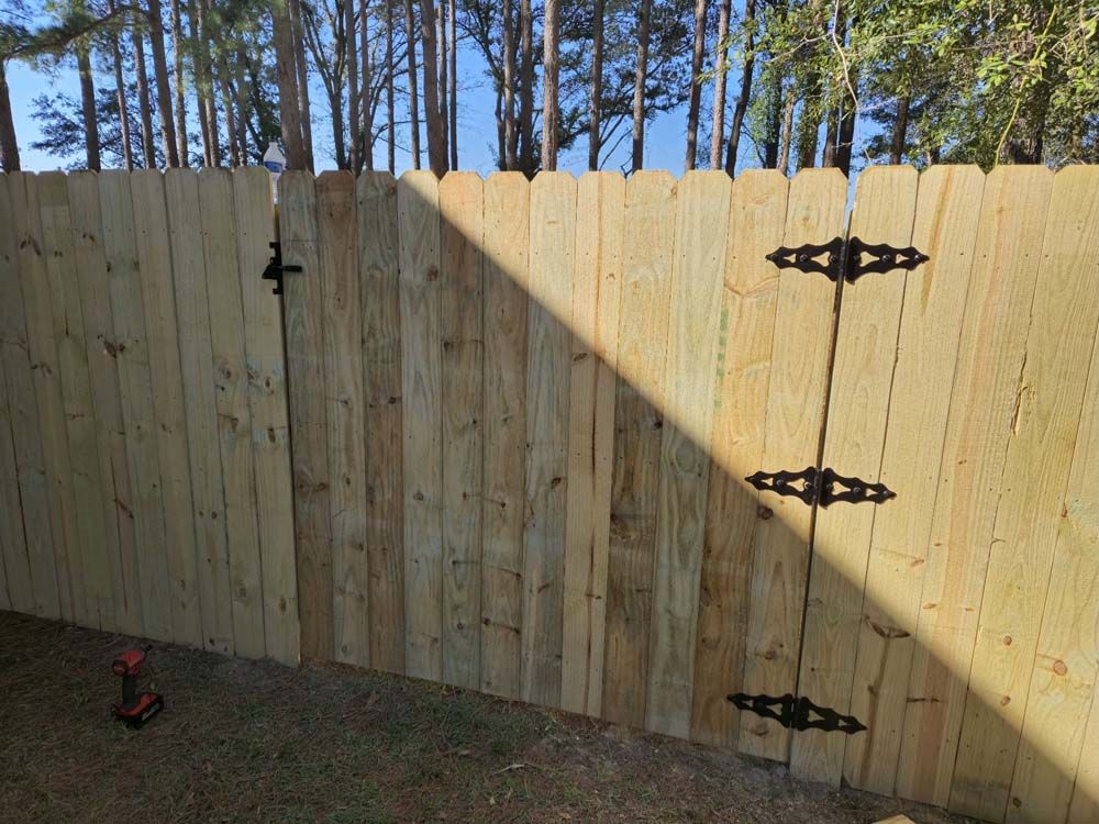 Wooden fence with a gate, black hinges and latch. Sunlight casts a shadow.