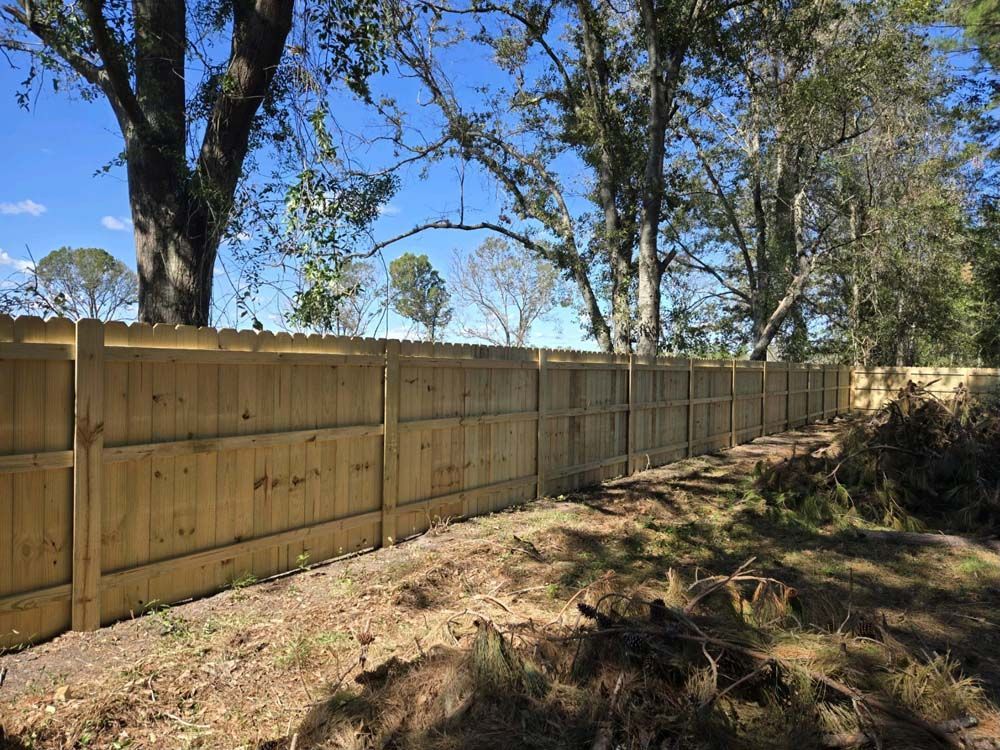 Wooden fence in a yard with trees and a blue sky in the background.