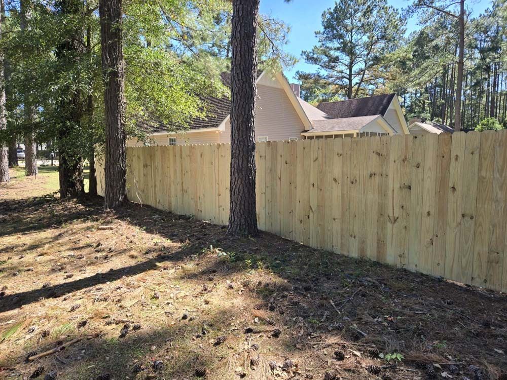 Wooden fence bordering a grassy area with trees and a house in the background.