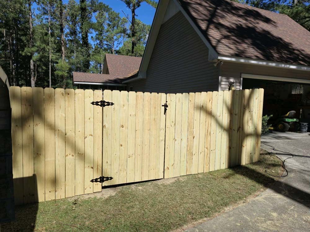 Wooden fence with two gates, in front of a house with a driveway.