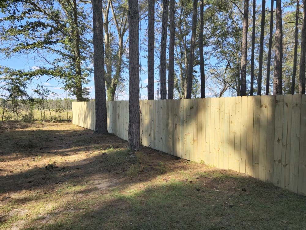 Wooden fence in a grassy area, trees in the background, blue sky.