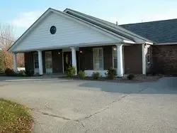 Low-angle view of a one-story brick building with a covered porch. White columns support the porch roof.
