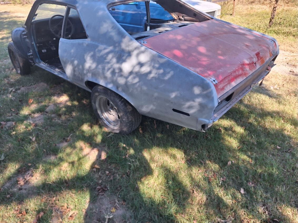 A gray car with a red hood is parked in the grass.