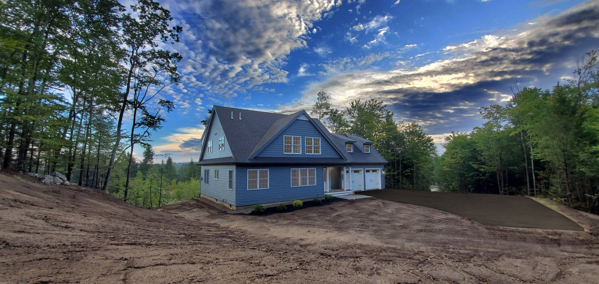 A blue house is sitting on top of a dirt hill surrounded by trees.