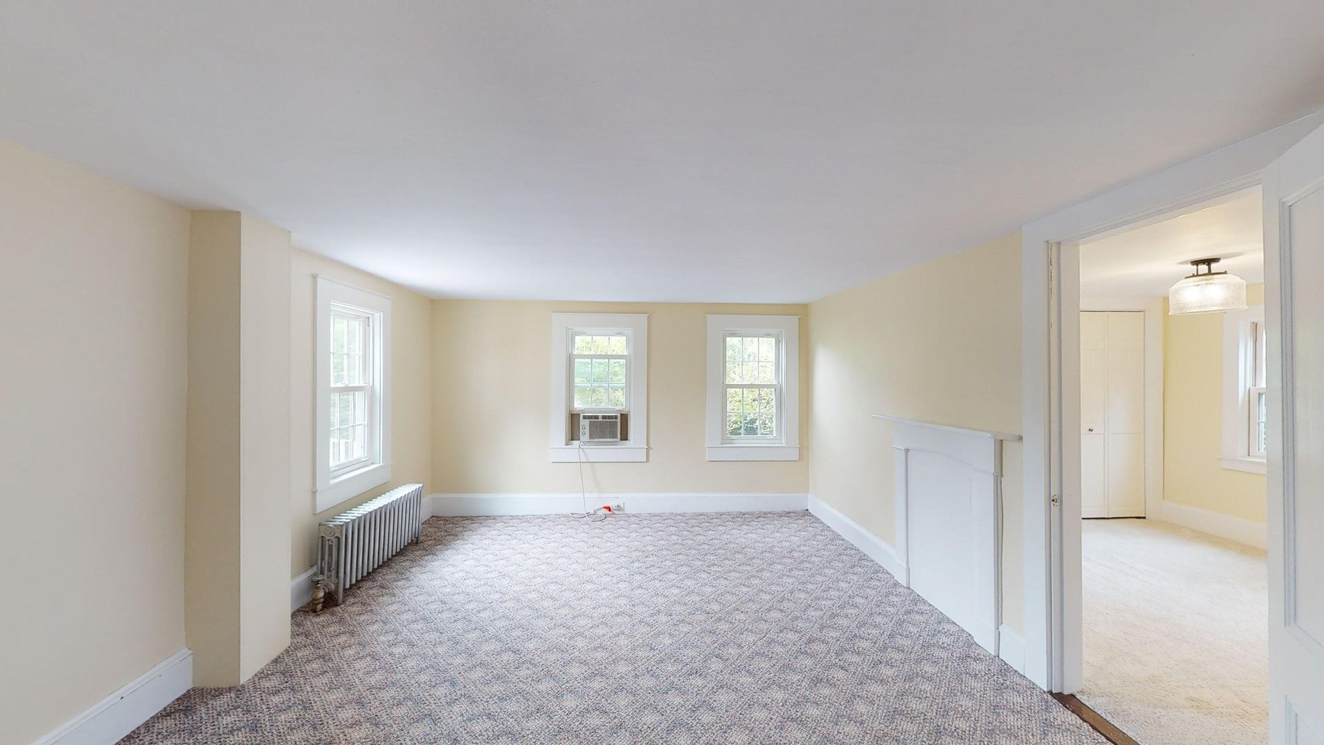 An empty living room with a carpeted floor and two windows.