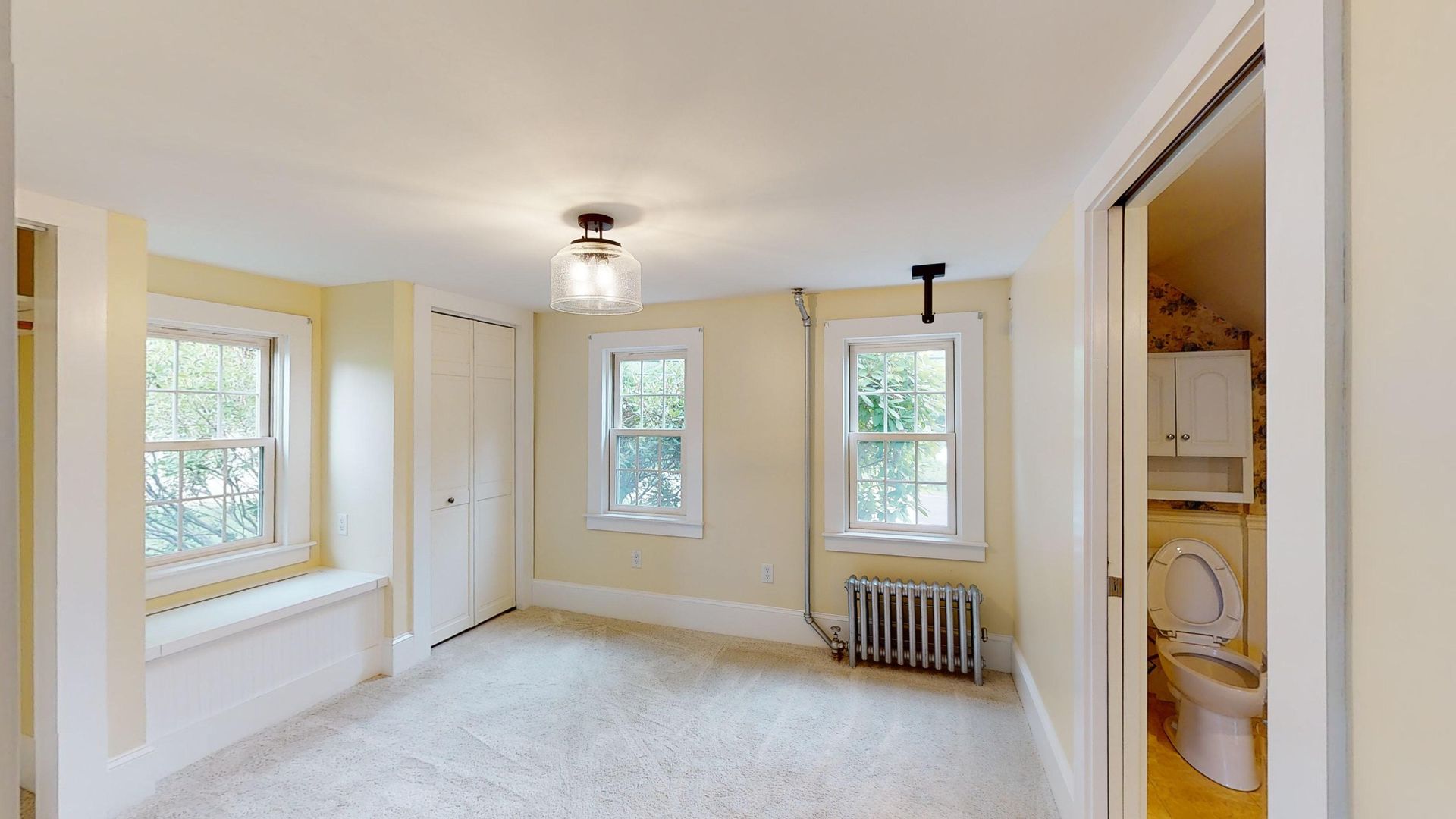 An empty room with a toilet , radiator , and window.