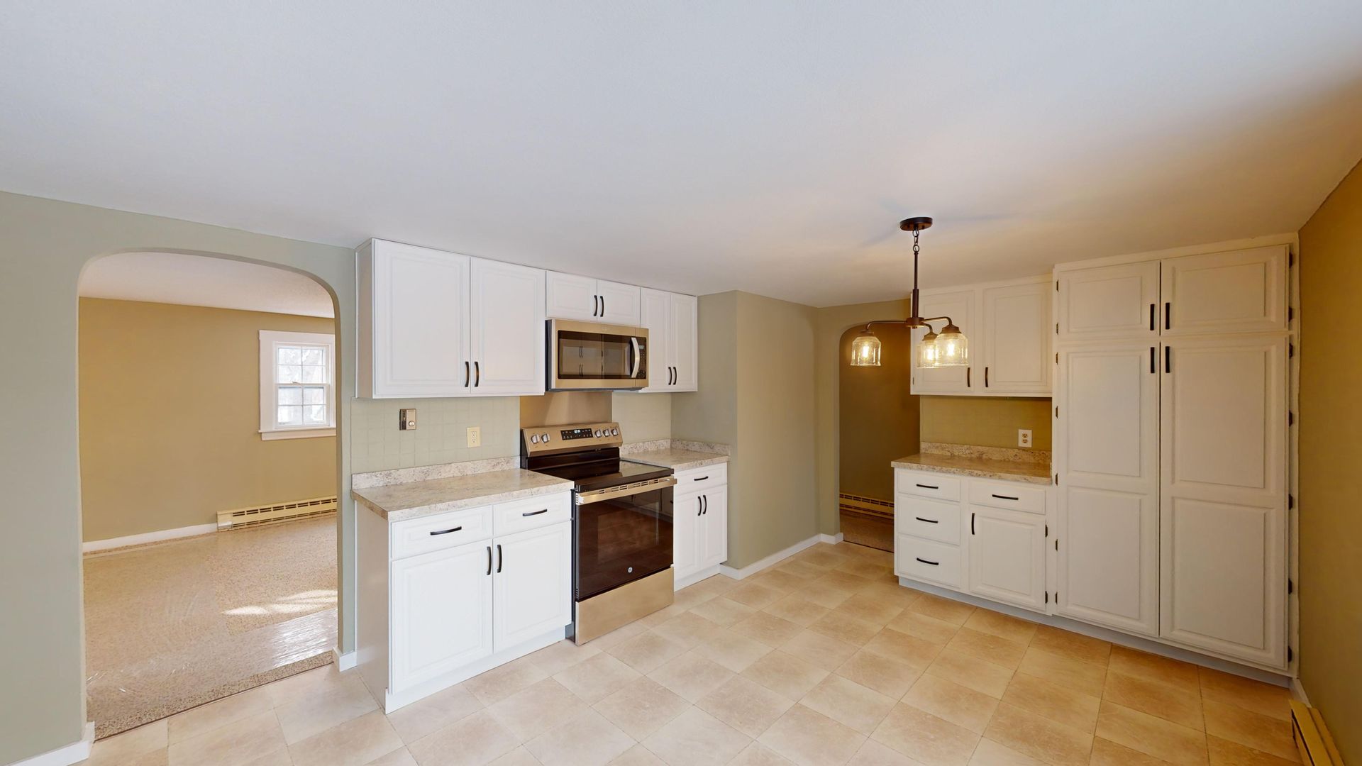 An empty kitchen with white cabinets and stainless steel appliances.