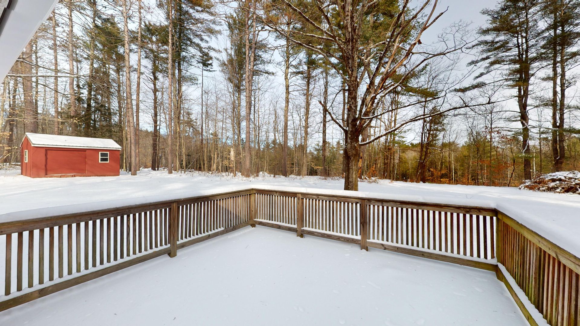 A snowy deck with a wooden railing and a red shed in the background.