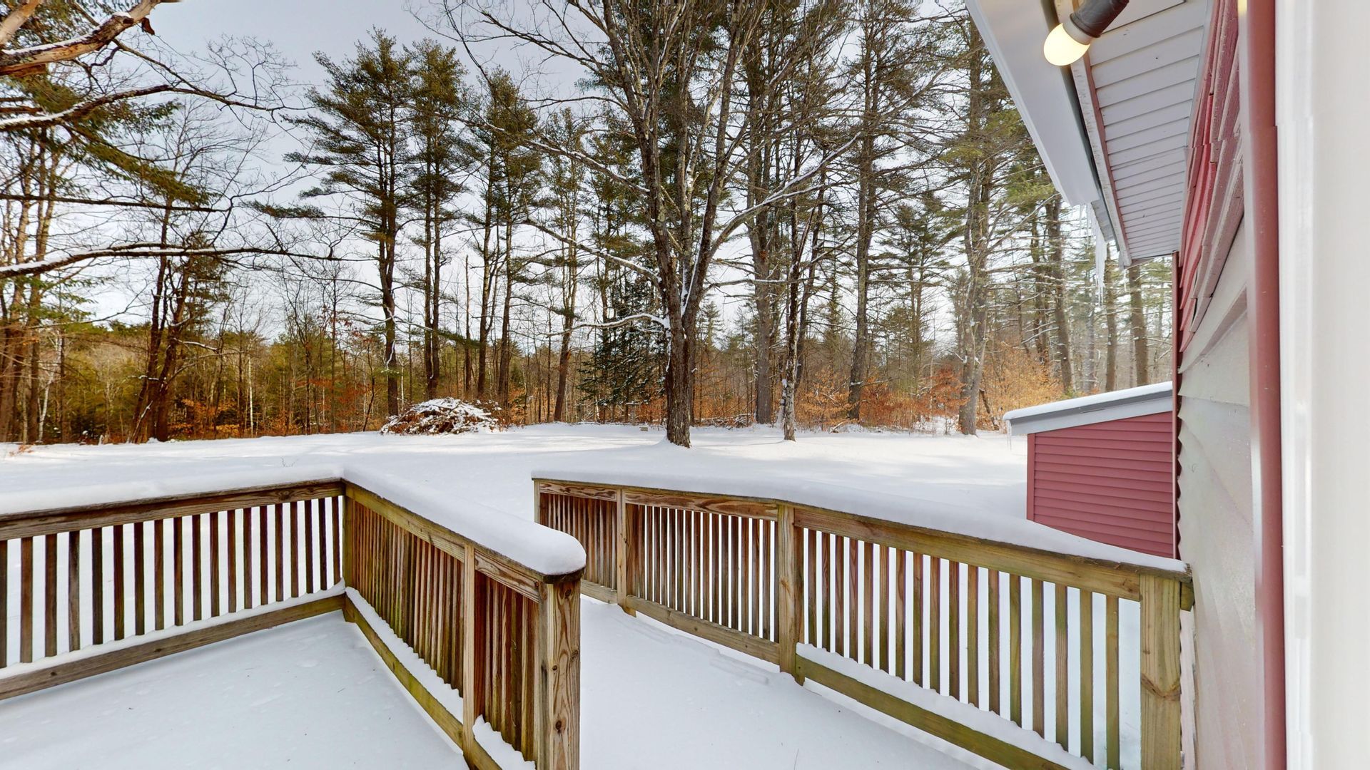 A snowy deck with a wooden railing and trees in the background.