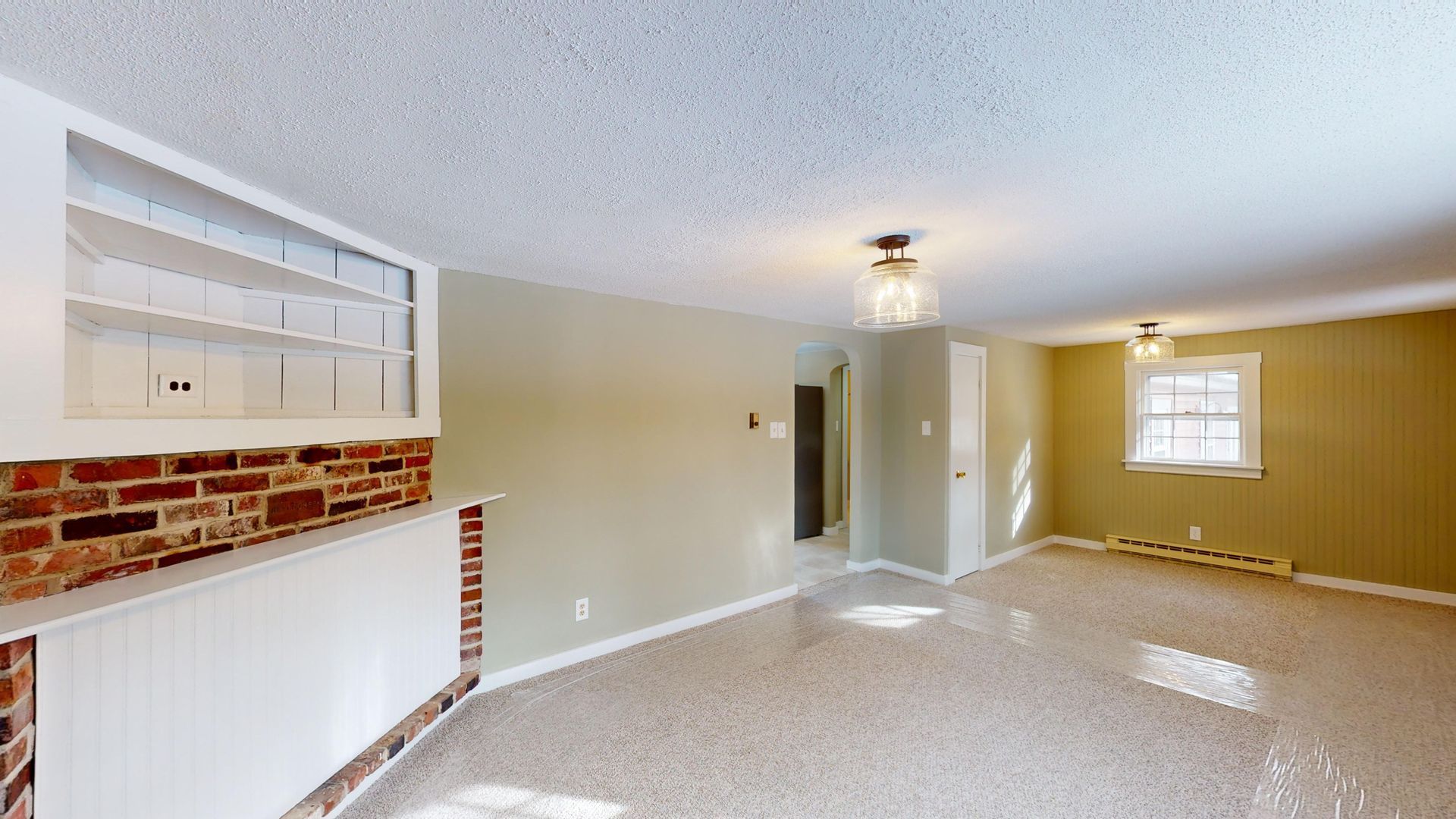 An empty living room with a brick fireplace and a window.