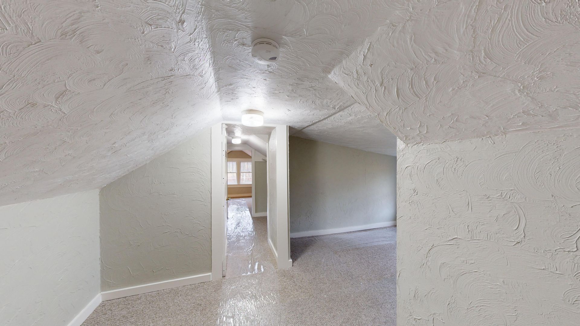 An empty attic with white walls and a carpeted floor.