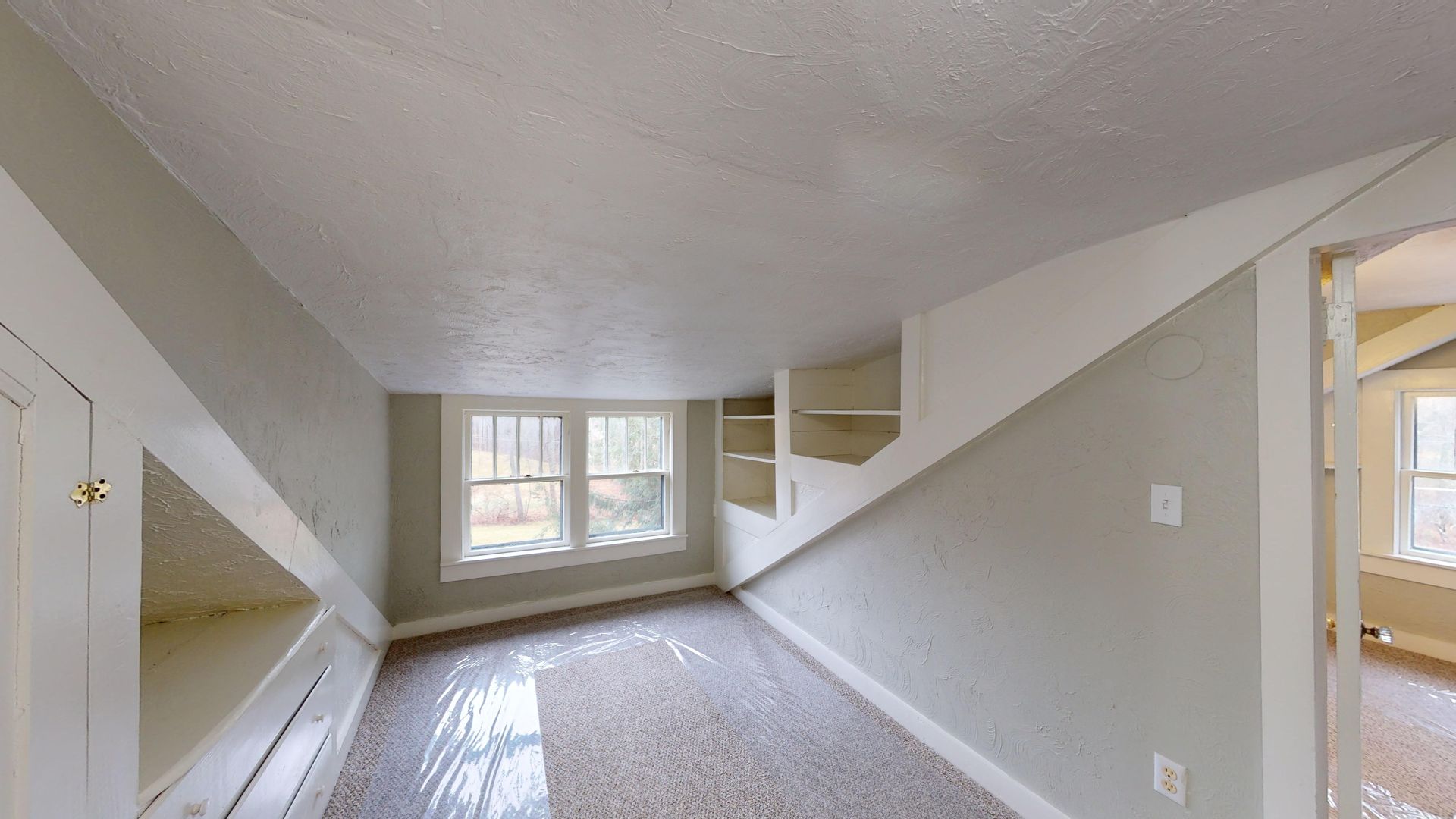 An empty room with a slanted ceiling and a window.