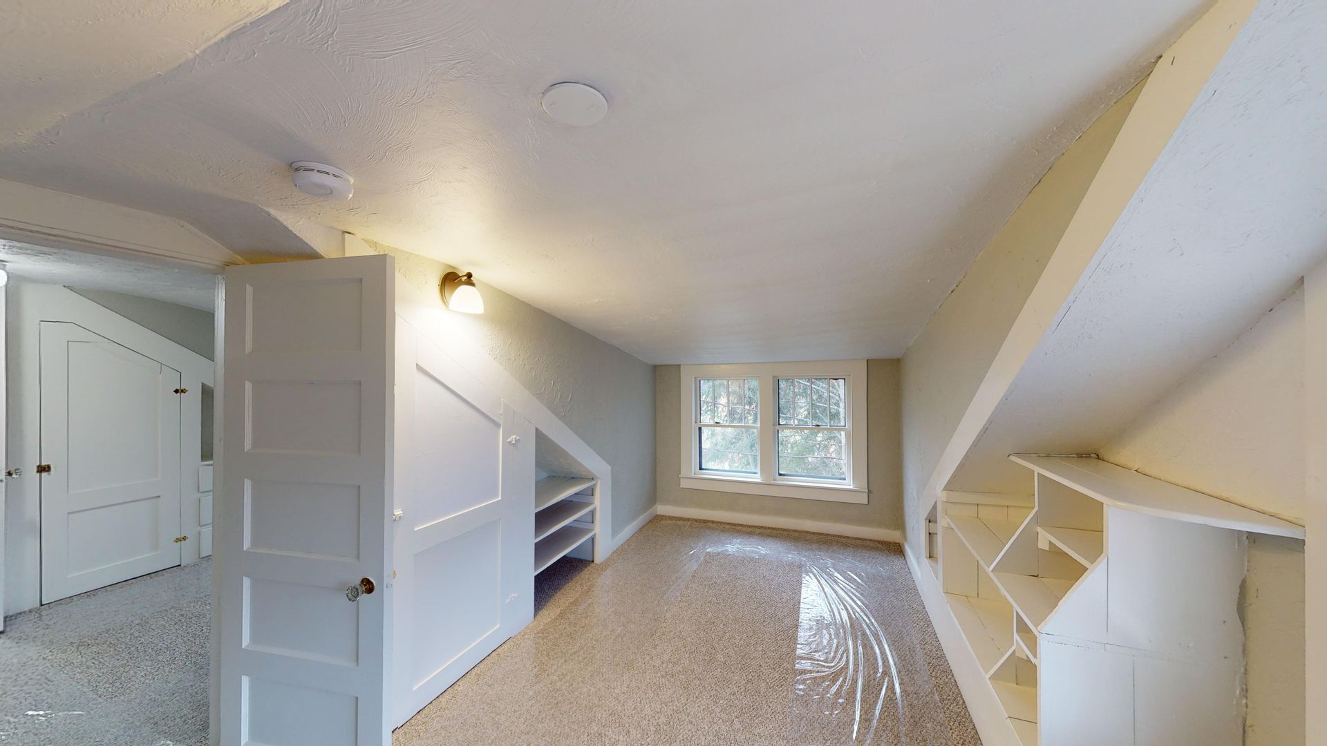 An empty room with a slanted ceiling and a white door.