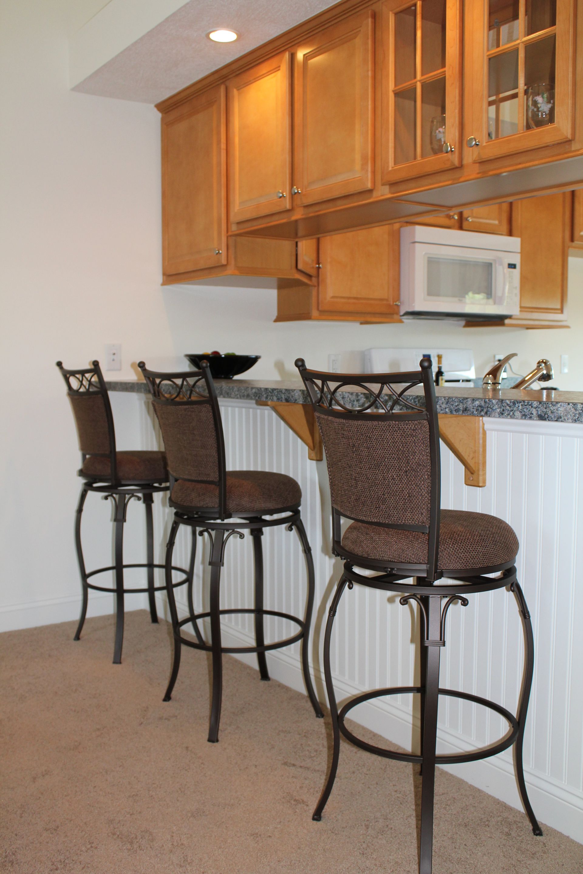 A kitchen with three bar stools and a microwave