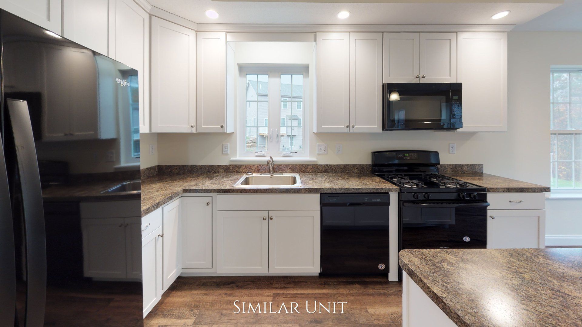 A kitchen with white cabinets , black appliances , granite counter tops and a window.