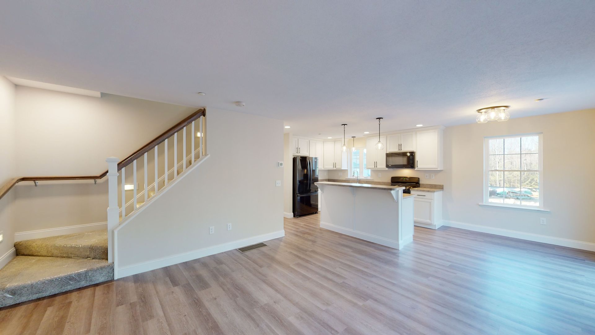 A living room with hardwood floors and stairs leading to a kitchen.