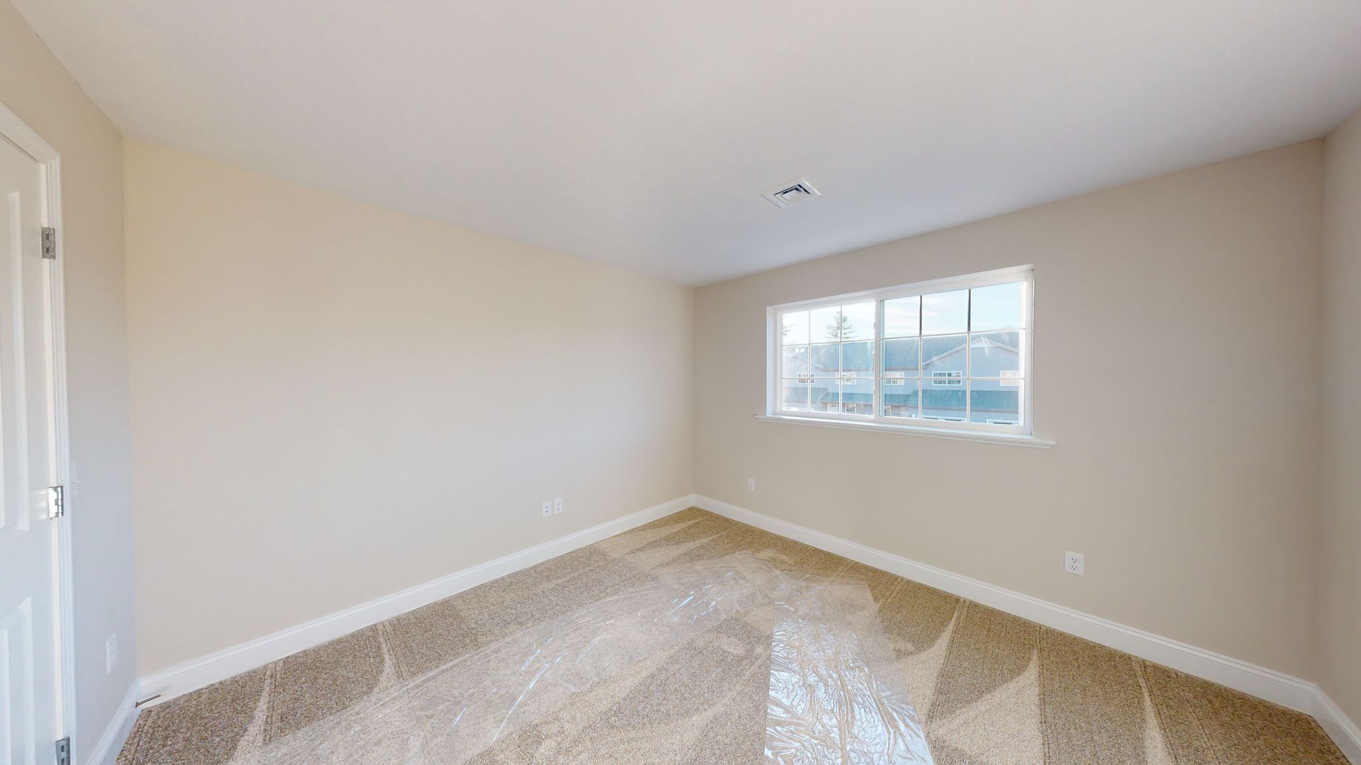 An empty bedroom with a window and a carpeted floor.