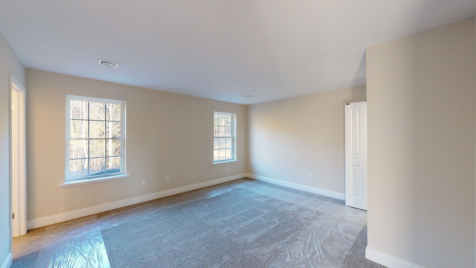 An empty bedroom with a carpeted floor and two windows.