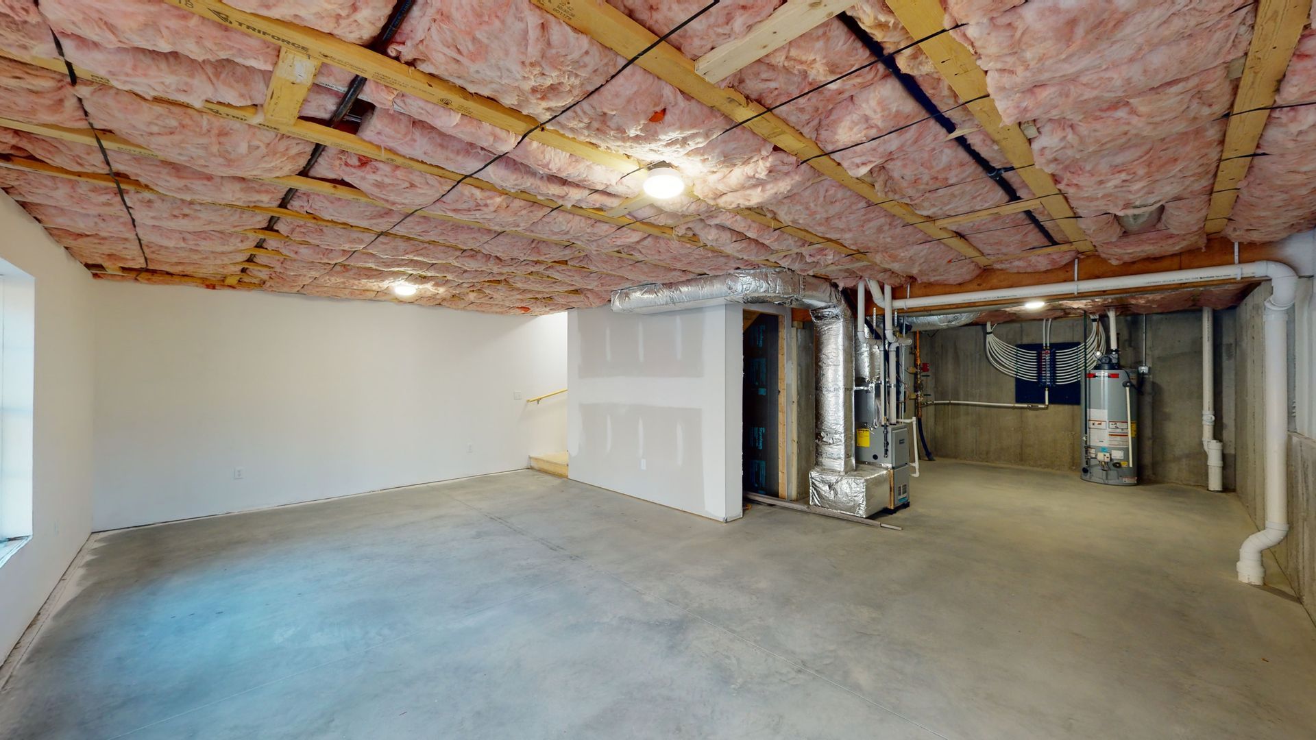 An empty basement with insulation on the ceiling and walls.