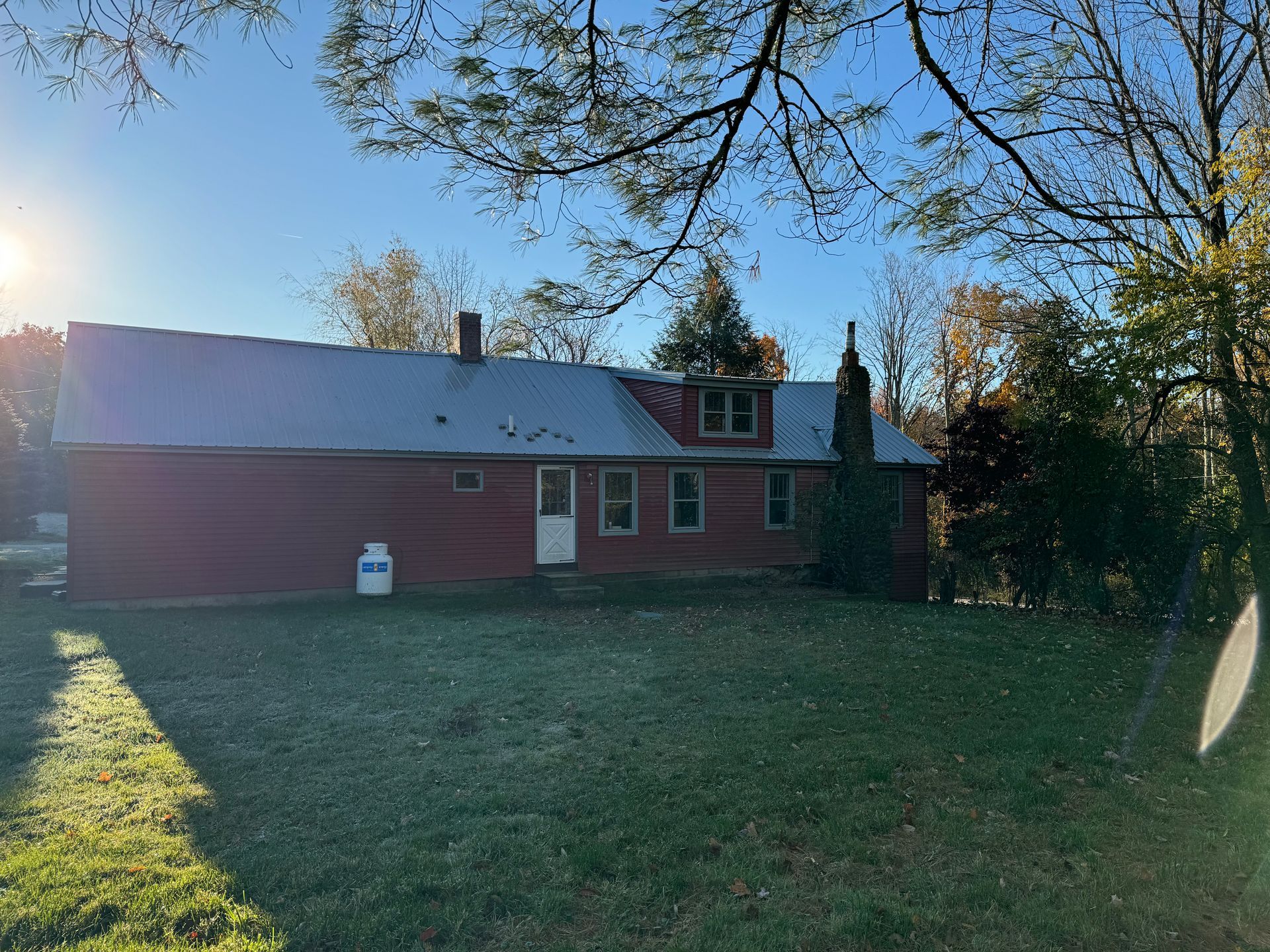 A red house with a white door is surrounded by trees and grass