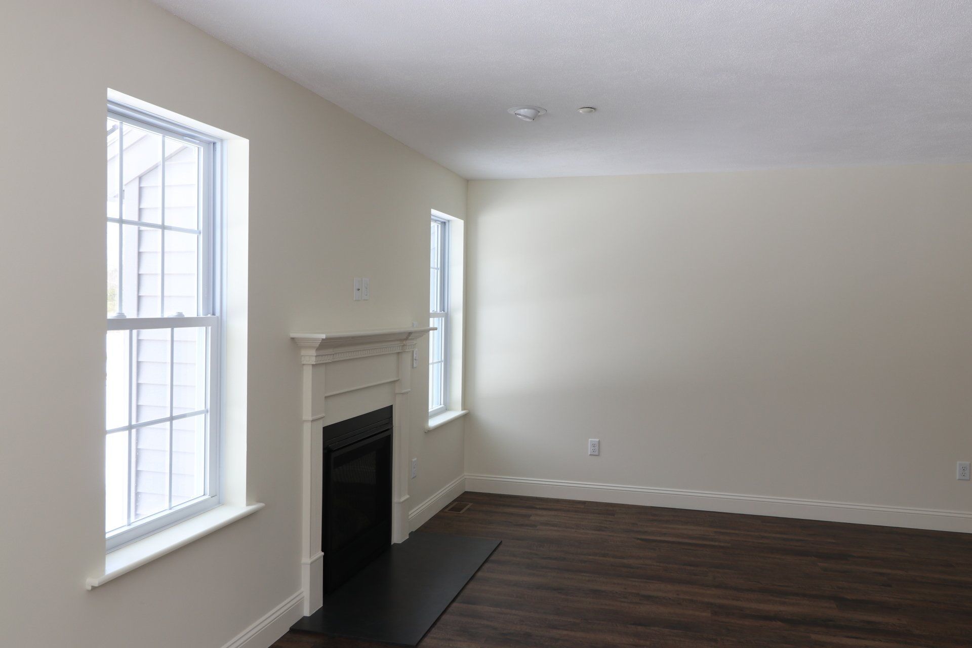 An empty living room with a fireplace and two windows.