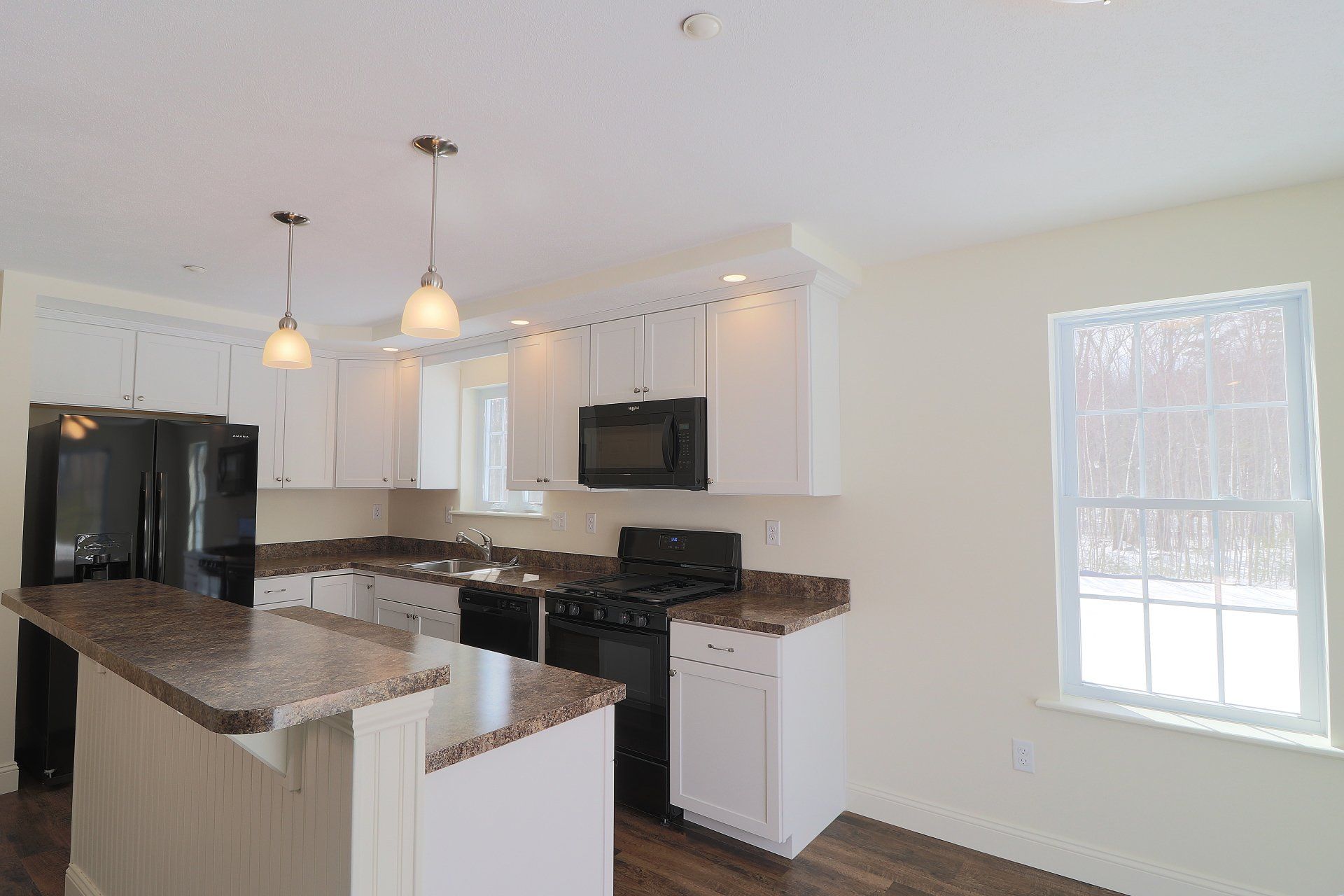 A kitchen with white cabinets , black appliances , granite counter tops and a large island.