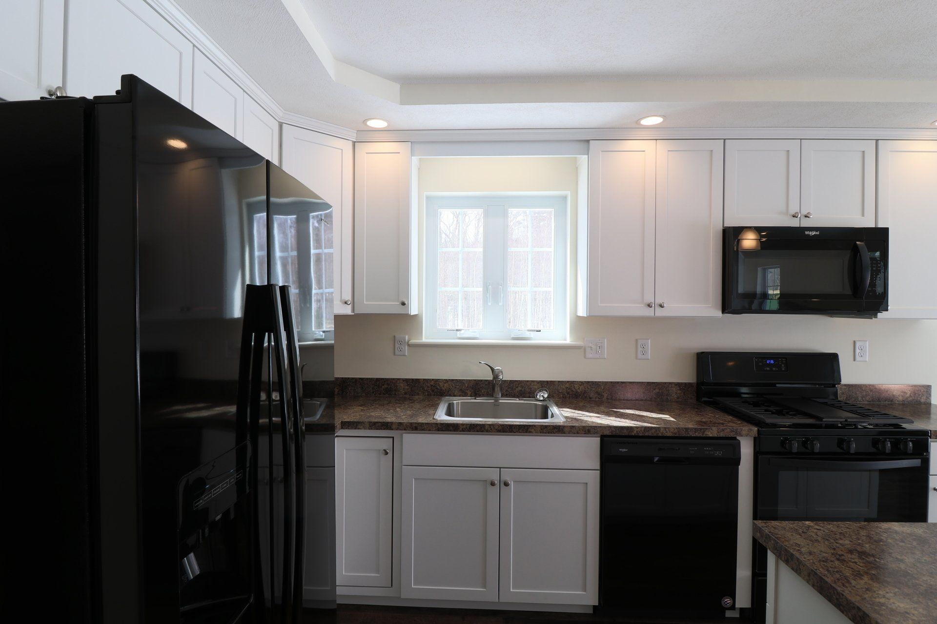 A kitchen with white cabinets , black appliances , a sink , and a window.