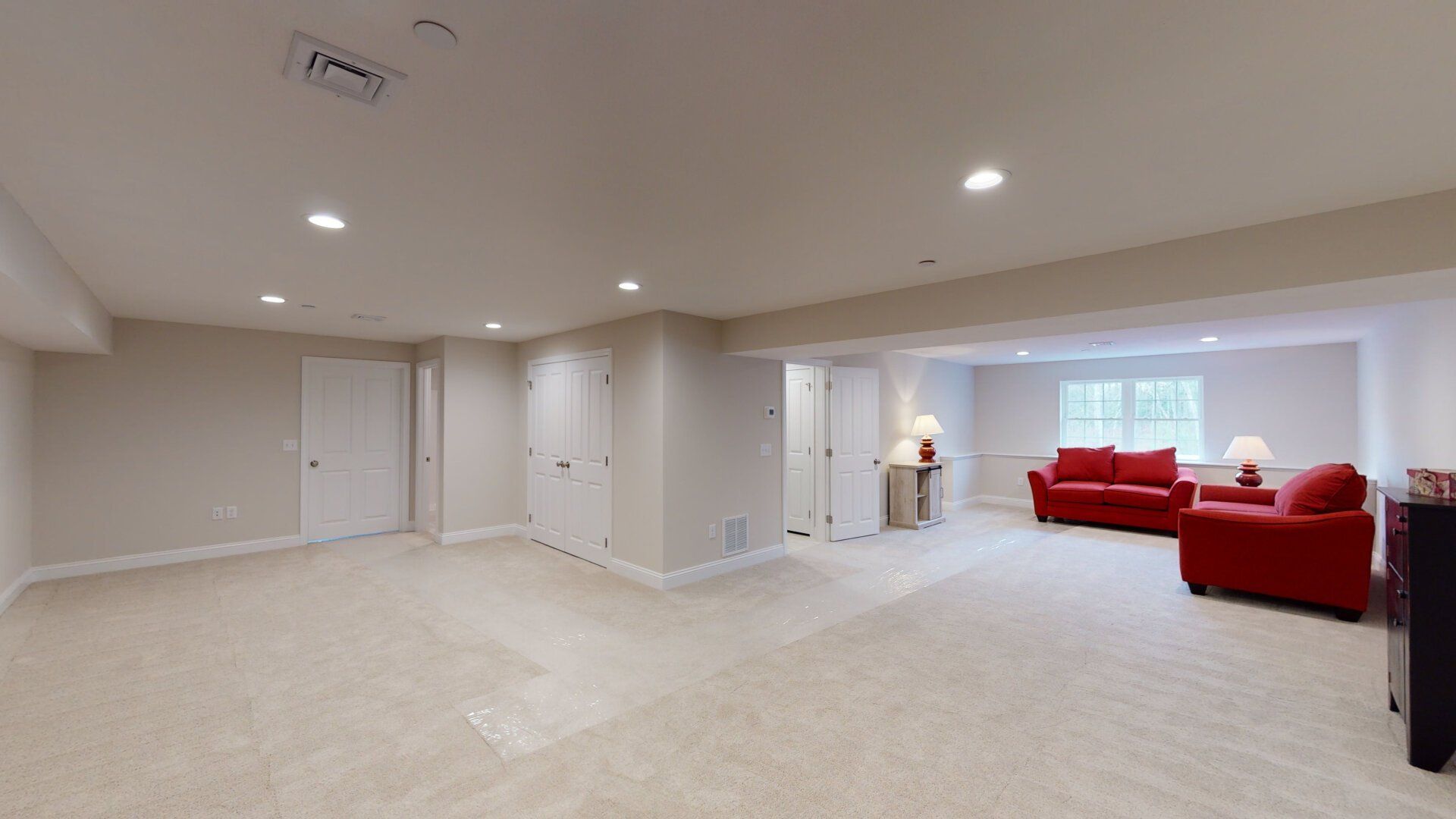 An empty basement with a couch and chairs in it.
