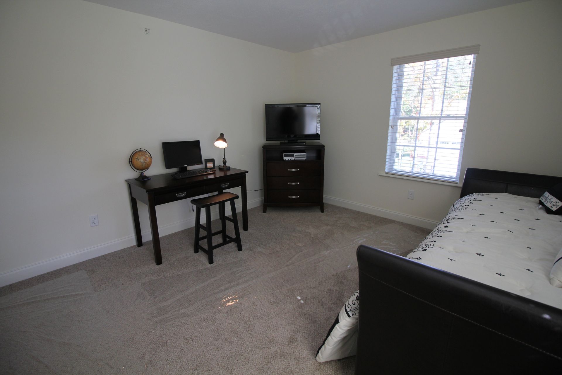 A bedroom with a bed , desk , television and dresser.