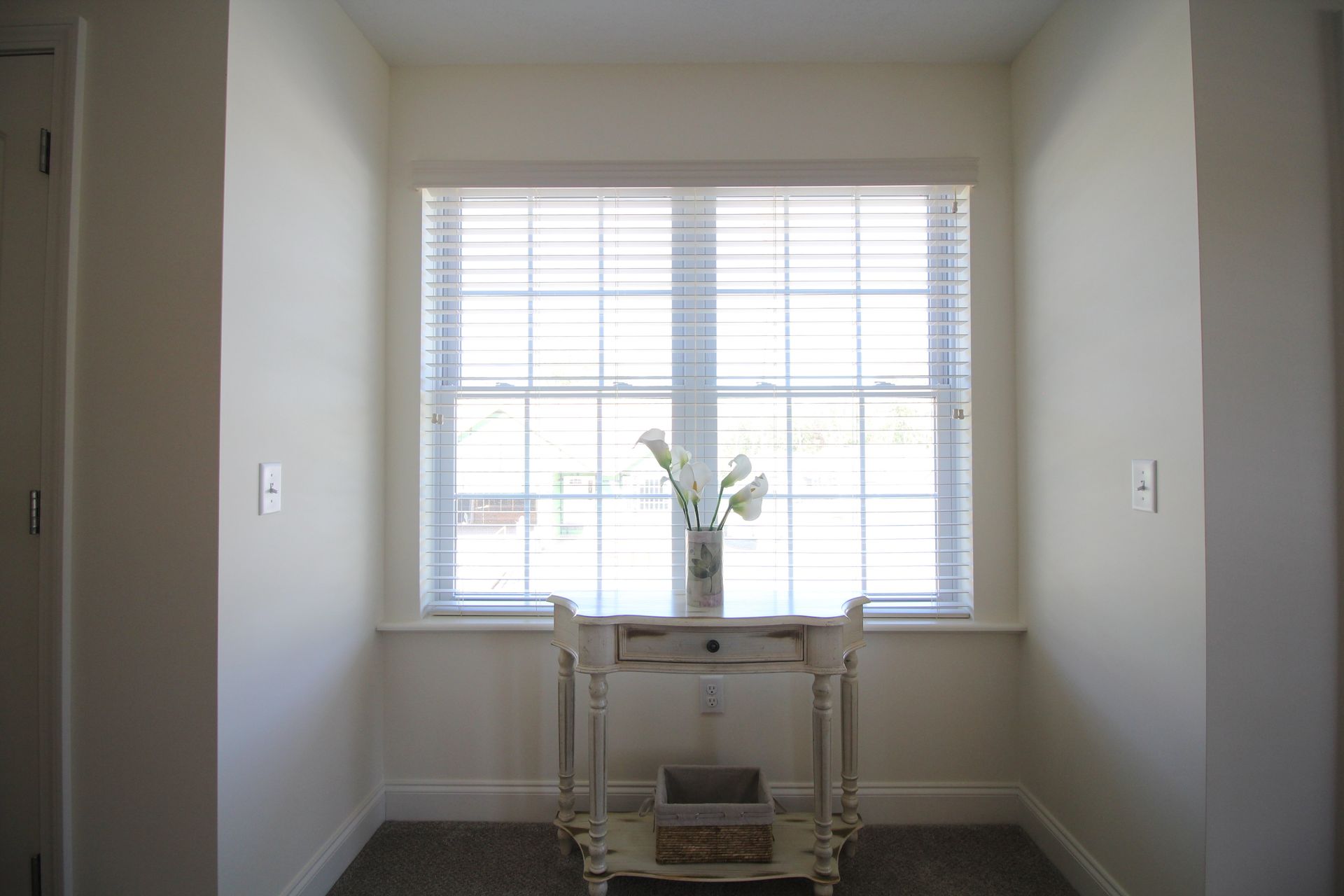 A white table with a vase of flowers on it in front of a window.