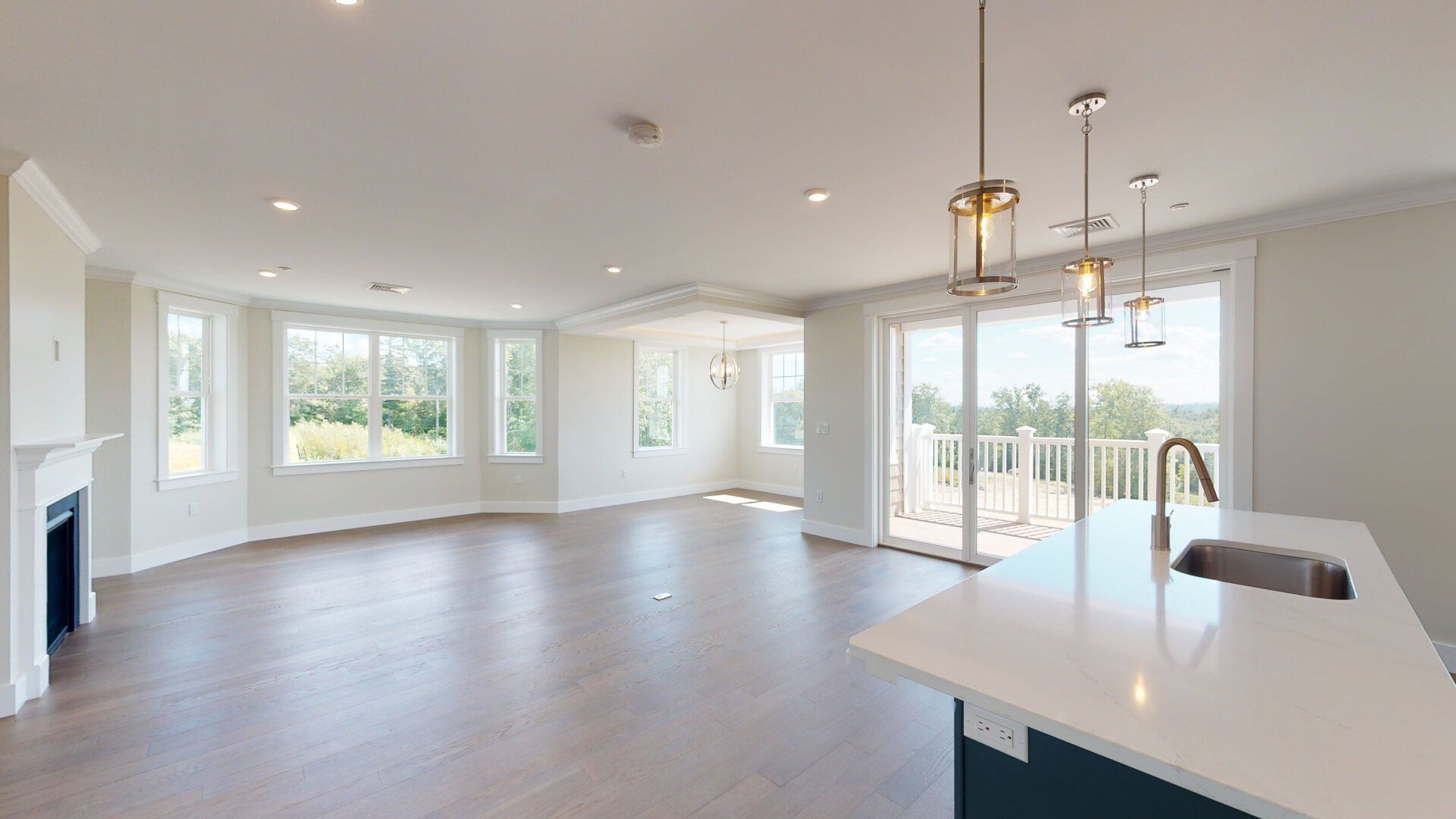 An empty living room with hardwood floors , a kitchen , and a fireplace.