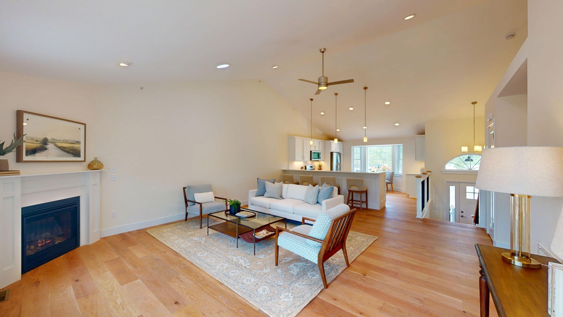 Bright open living room with hardwood floors, white sofa, blue fireplace, and dining area in the background