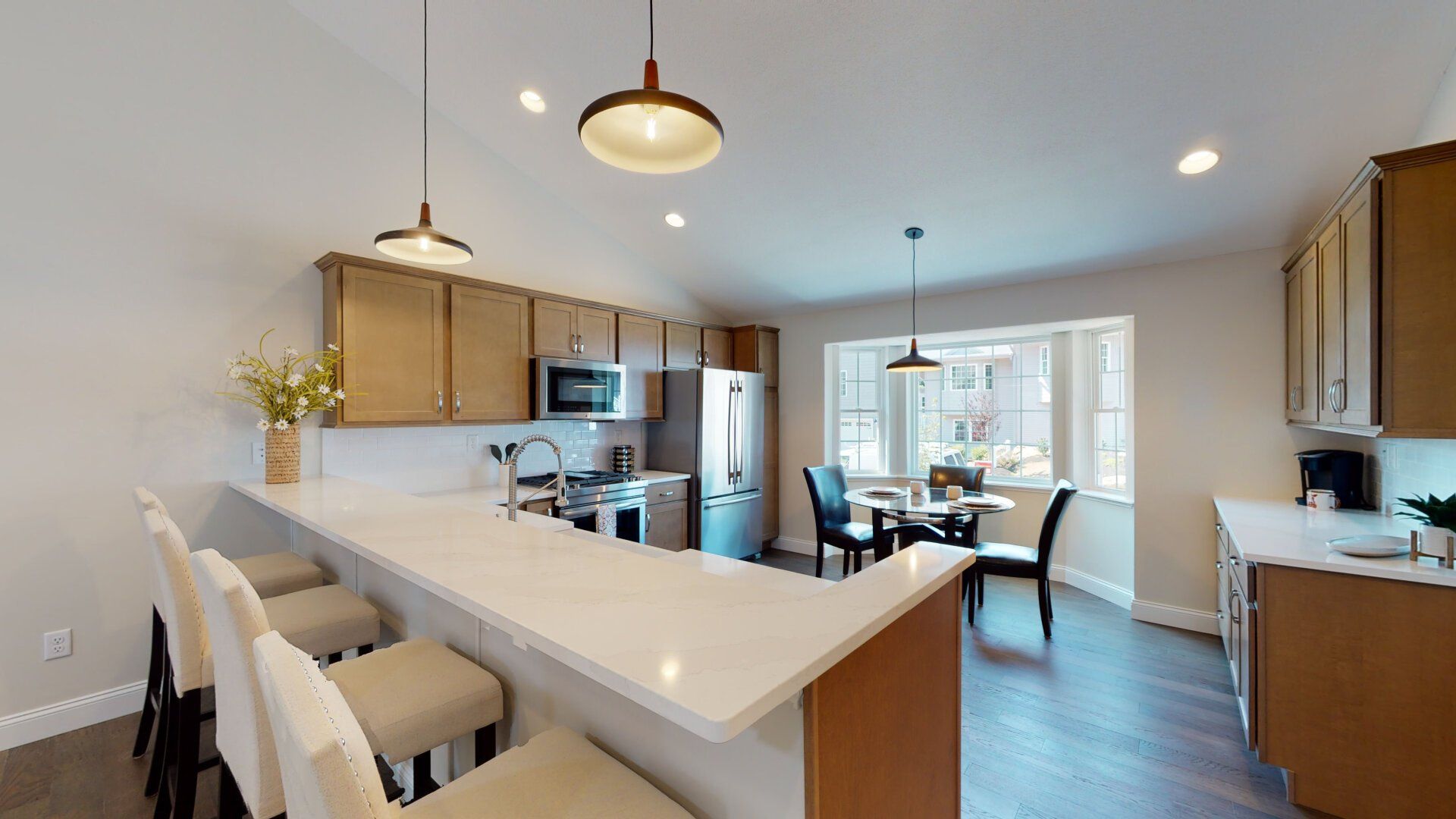 A kitchen with a bar and stools and a dining room in the background.