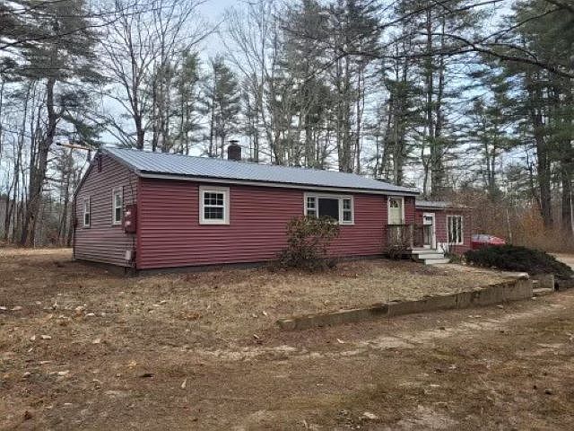 A red house is sitting on top of a dirt field in the middle of a forest.