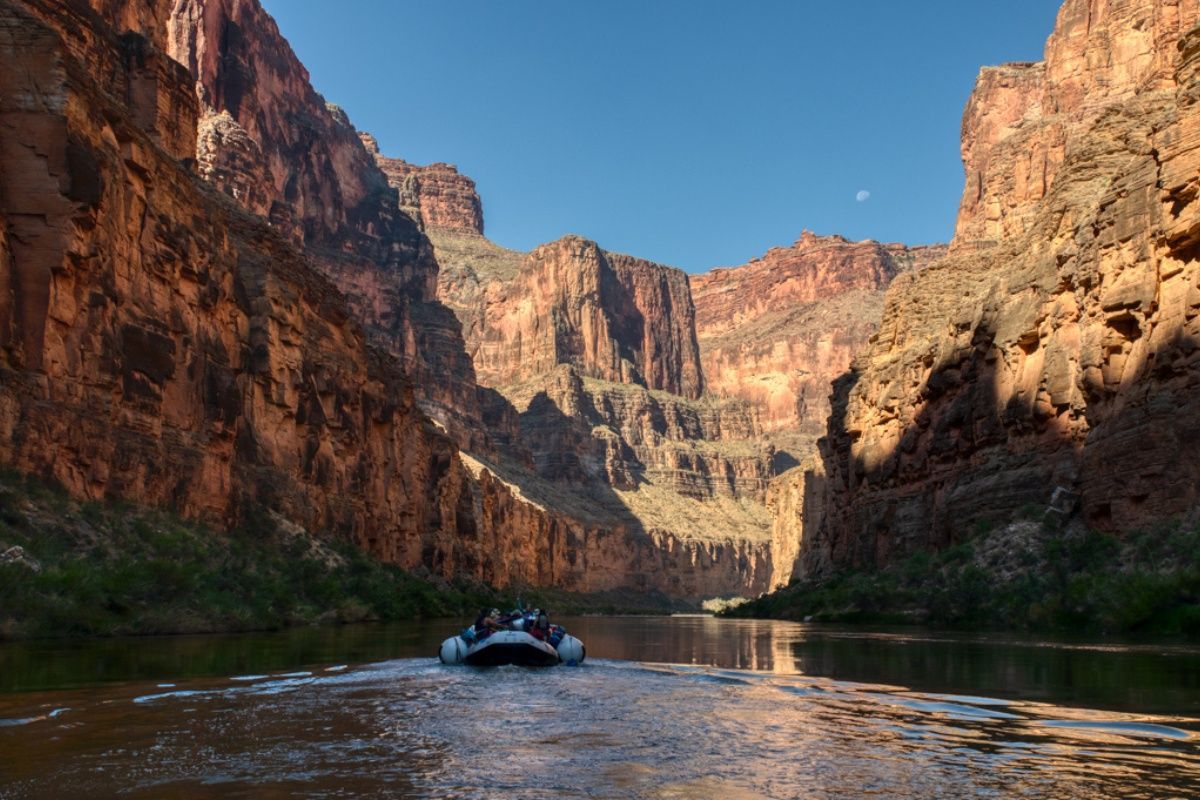 A boat is floating down a river in the middle of a canyon.