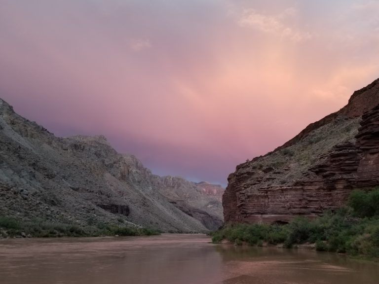A river flowing through a canyon with mountains in the background and a pink sky