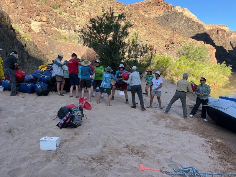 A group of people are standing in the sand near a river