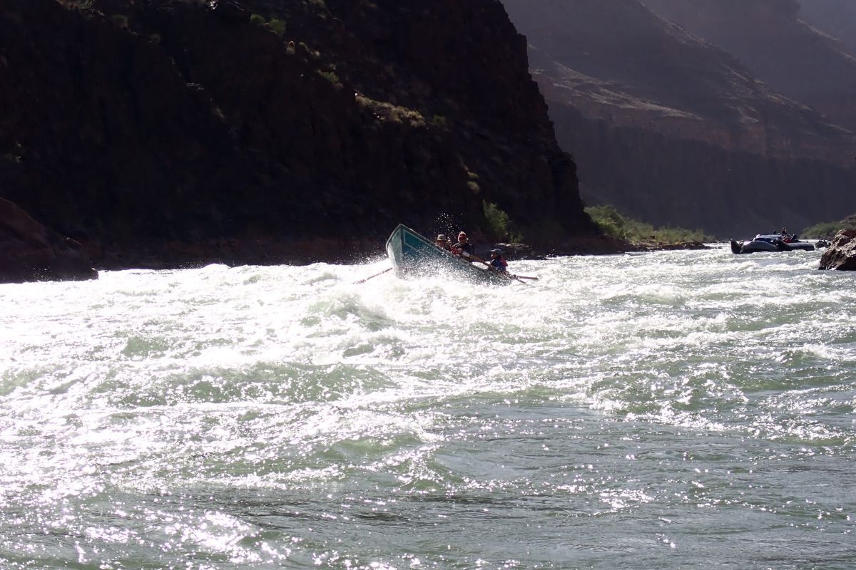Raft navigating whitewater rapids, with mountain backdrop. Sunlit water, guide paddling.