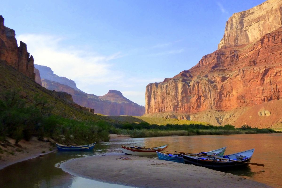 A group of kayaks are sitting on the shore of a river.
