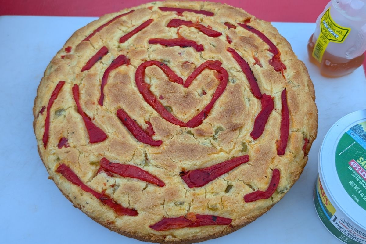 Cornbread decorated with red peppers arranged in a heart and circular pattern, on a white surface.
